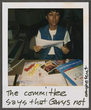 Primary view of [Woman sitting at a desk, holding documents]