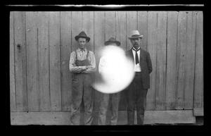 Primary view of [Photo of three men standing in front of a fence]
